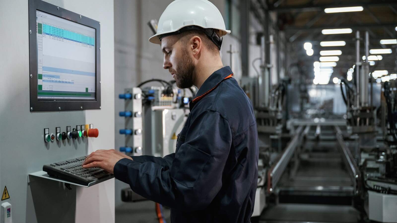Operario con casco consultando en la pantalla del puesto los datos de producción junto a una línea automática