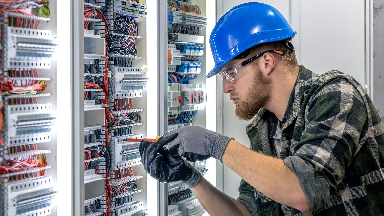 Técnico con casco y gafas conectando el cableado de un armario eléctrico de control con PLC y bornas